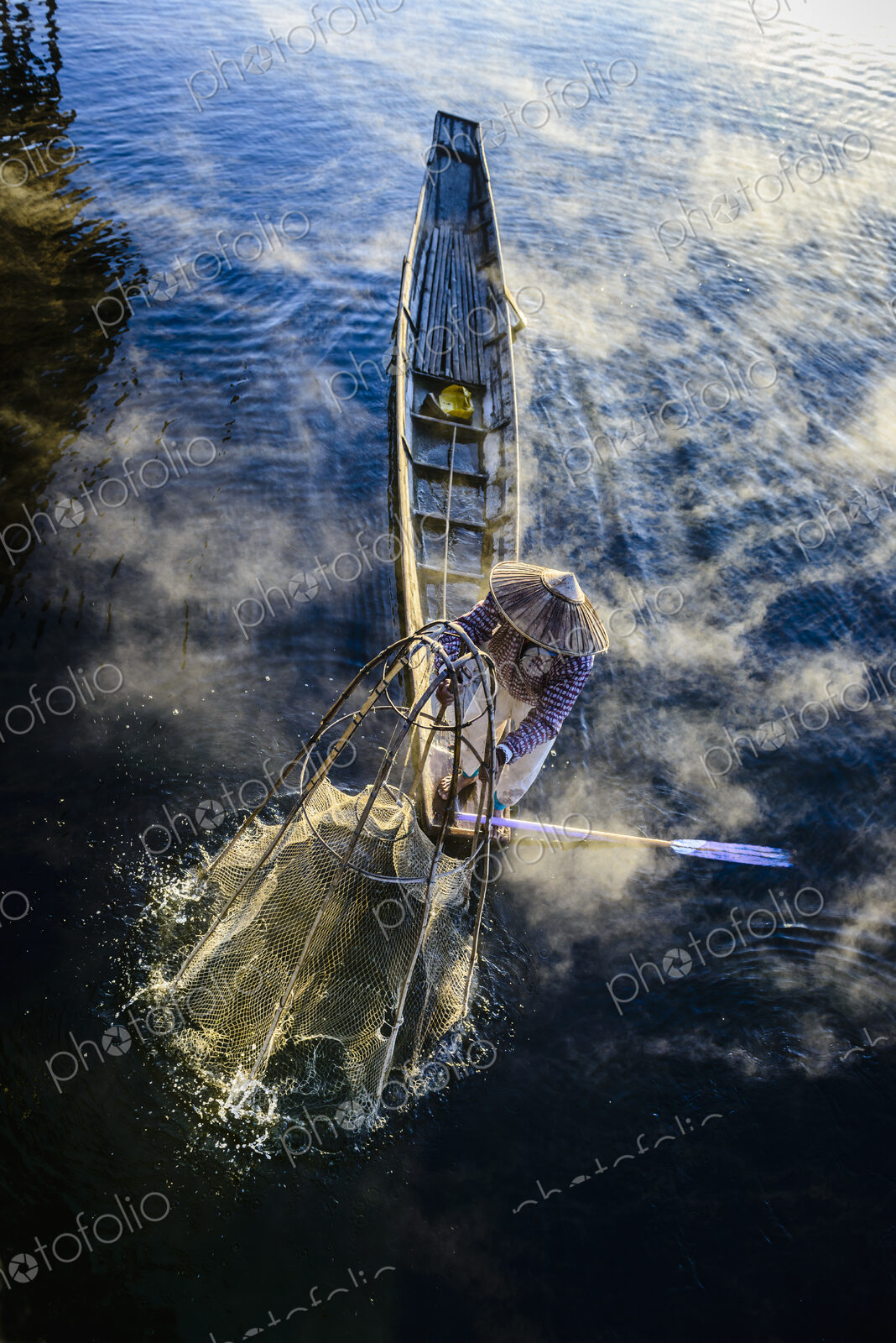 High angle view of Asian fisherman using fishing net in canoe on river