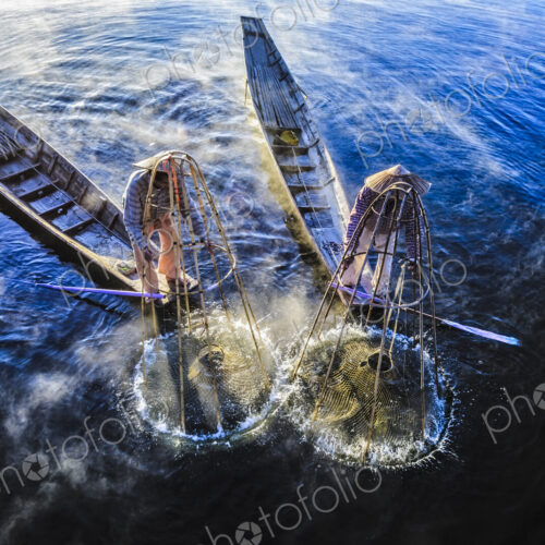 High angle view of Asian fishermen using fishing net in canoes on river High angle view of Asian fishermen using fishing net in canoes on river