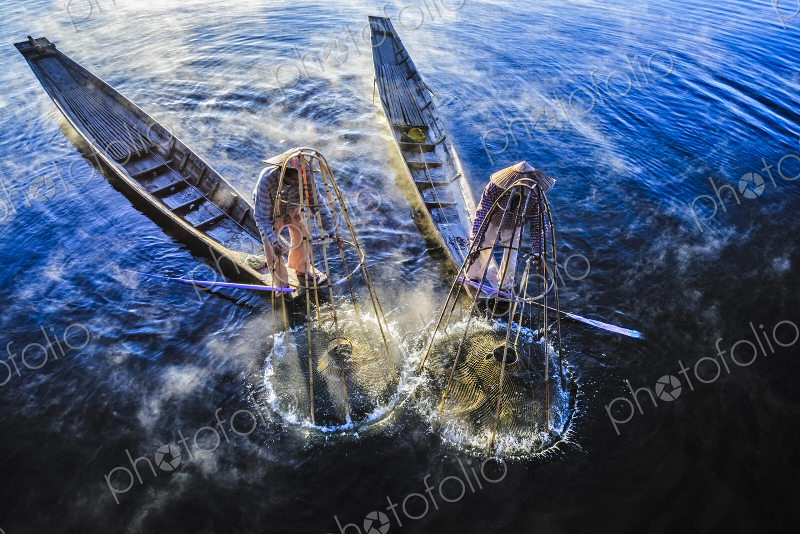 High angle view of Asian fishermen using fishing net in canoes on river