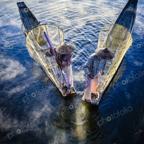 High angle view of Asian fishermen using fishing nets in canoe on river High angle view of Asian fishermen using fishing nets in canoe on river
