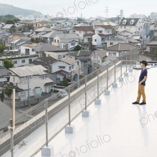 High angle view of Japanese man standing on a rooftop in an urban setting.