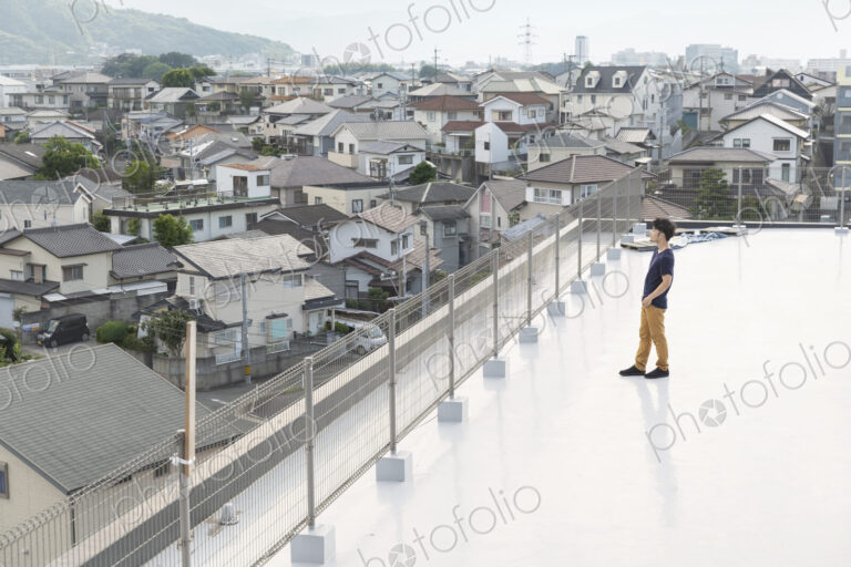 High angle view of Japanese man standing on a rooftop in an urban setting.
