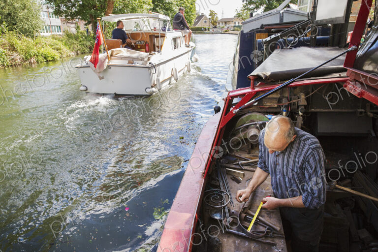High angle view of a blacksmith working at his bench on a narrowboat on the water,…