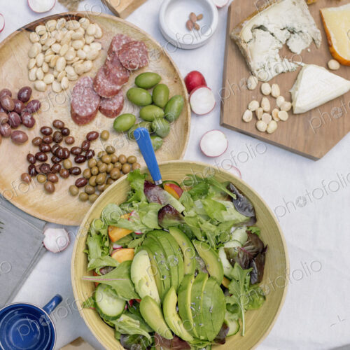 High angle view of a cheese board, cheese, olives, nuts and a bowl of salad on a table.
