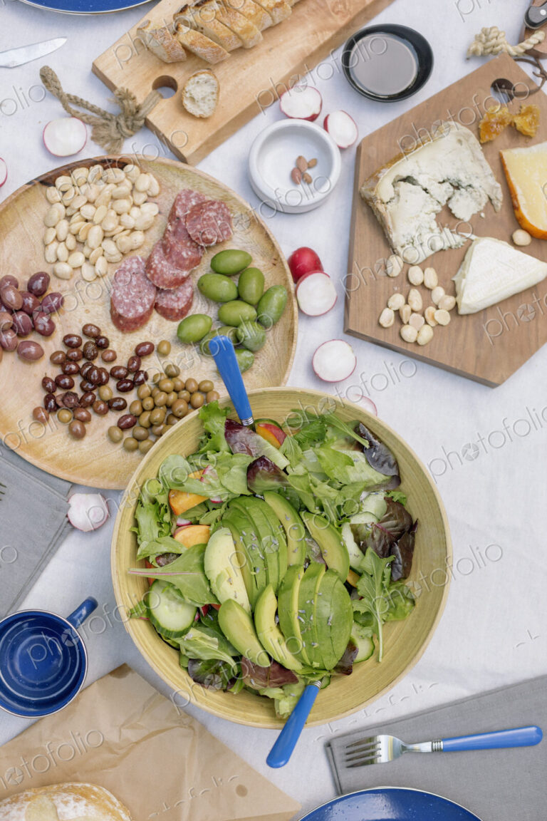 High angle view of a cheese board, cheese, olives, nuts and a bowl of salad on a table.