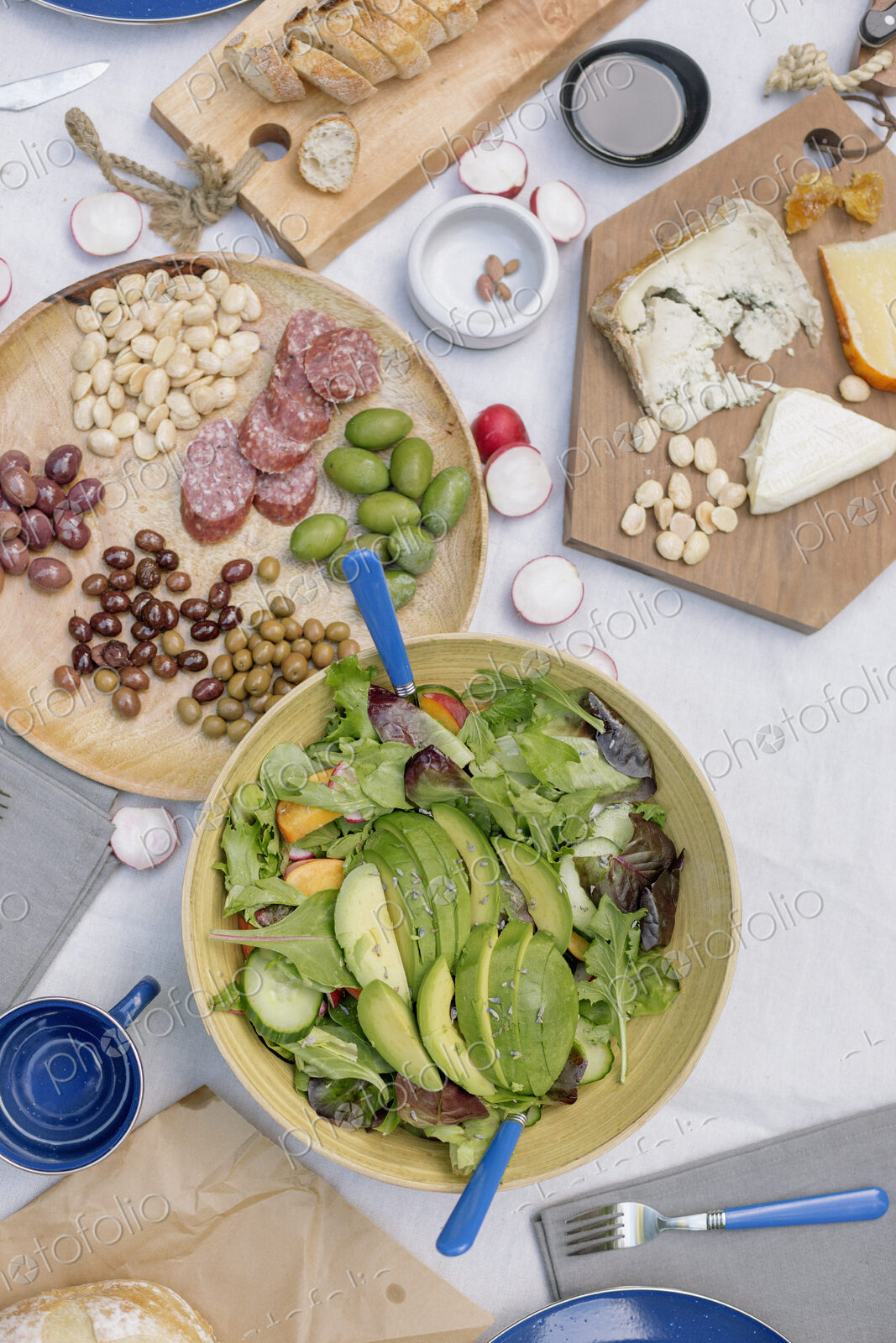 High angle view of a cheese board, cheese, olives, nuts and a bowl of salad on a table.