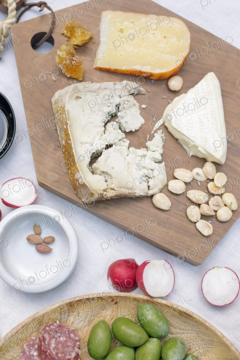High angle view of a cheese board, cheese, olives, nuts and radishes on a table.