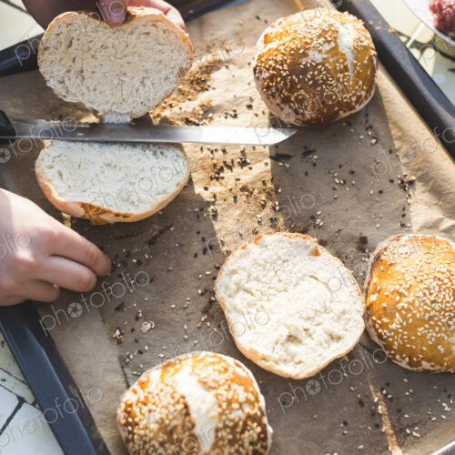 High angle view of a child standing at a table, slicing hamburger buns.