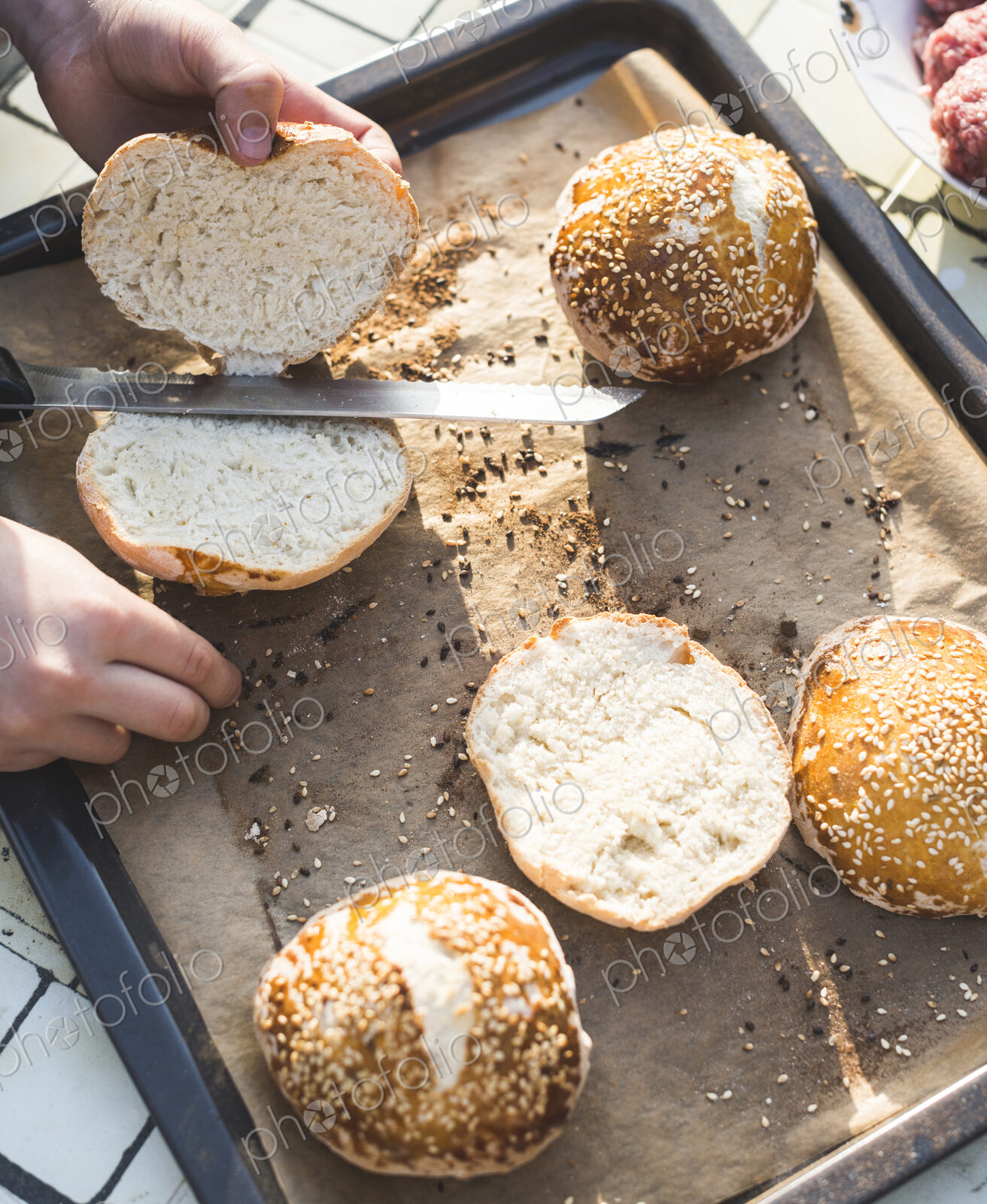 High angle view of a child standing at a table, slicing hamburger buns.
