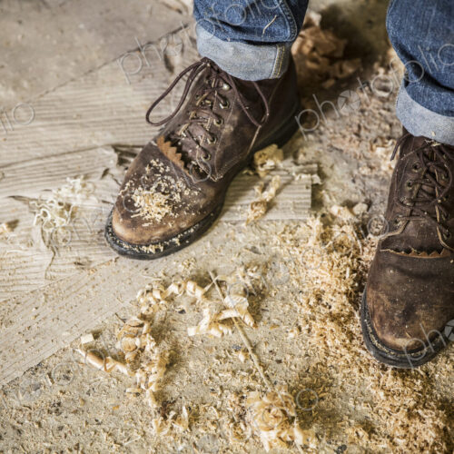 High angle view of a man wearing jeans and brown leather boots standing in a workshop,…