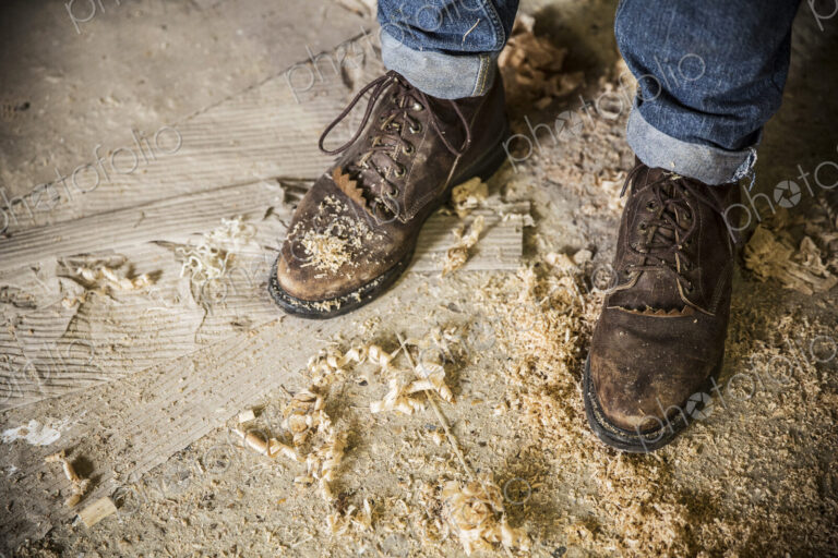 High angle view of a man wearing jeans and brown leather boots standing in a workshop,…
