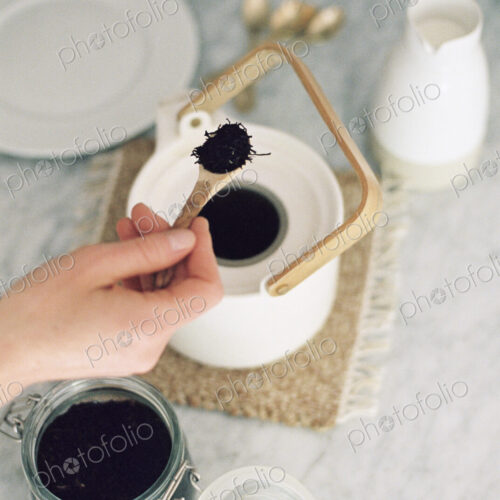High angle view of a tea pot and a glass jar with tea leaves, woman preparing tea.