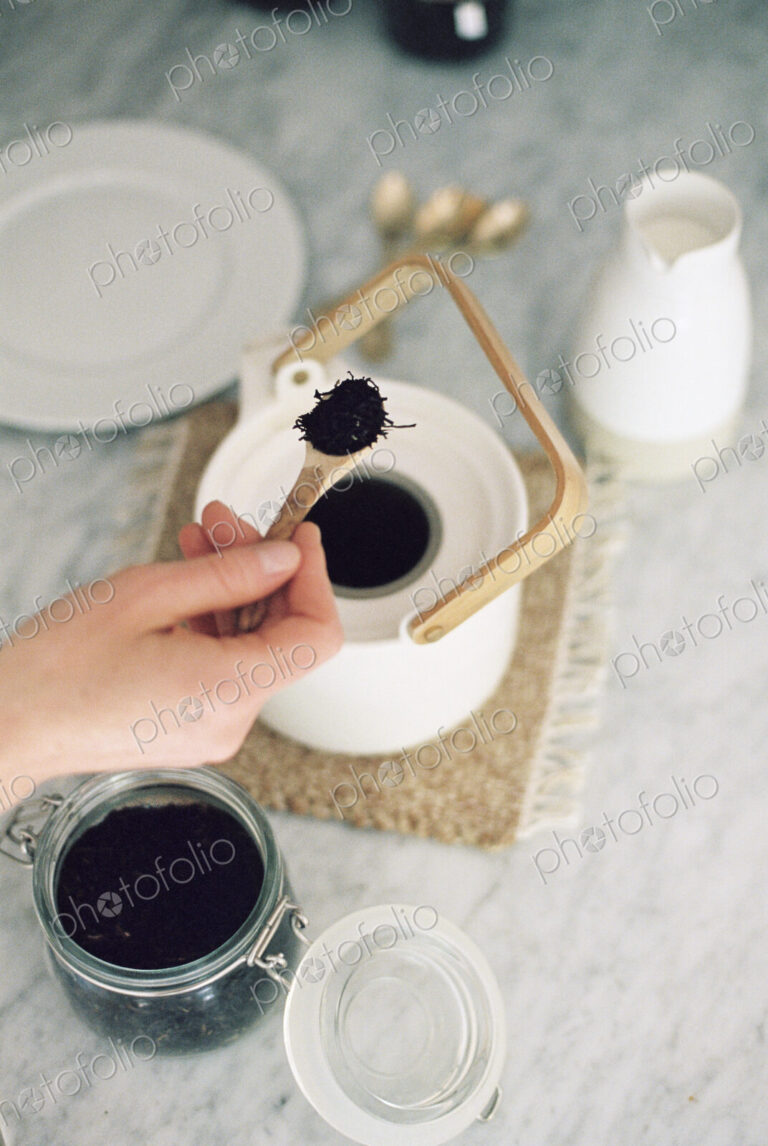 High angle view of a tea pot and a glass jar with tea leaves, woman preparing tea.