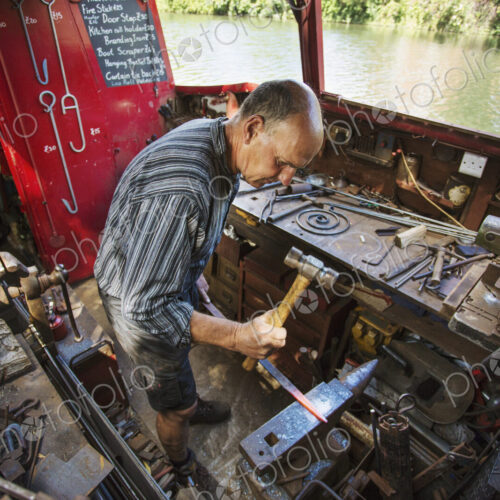 High angle view of blacksmith at his workbench on his working boat on the water,… High angle view of blacksmith at his workbench on his working boat on the water,…