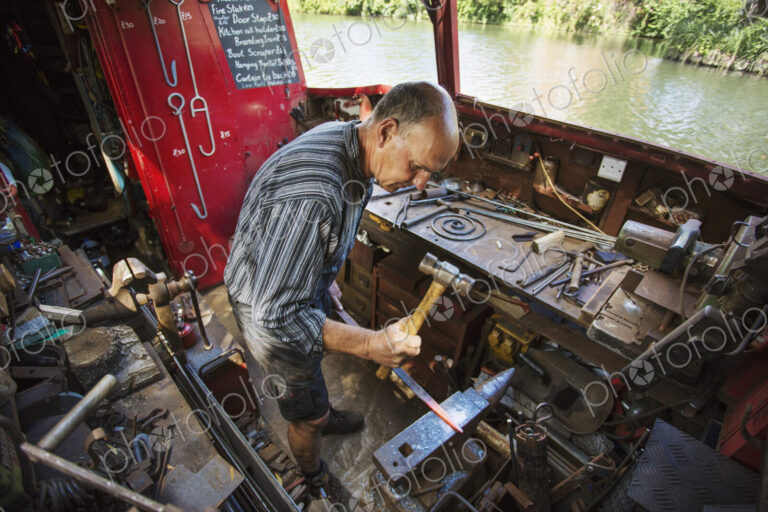 High angle view of blacksmith at his workbench on his working boat on the water,…