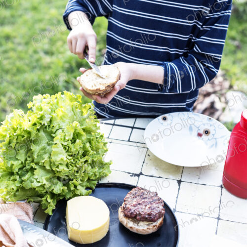 High angle view of child standing at a table in a garden, preparing a hamburger.