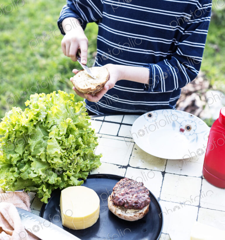High angle view of child standing at a table in a garden, preparing a hamburger.