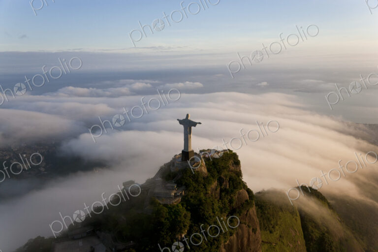 High angle view of colossal Christ Redeemer statue surrounded by clouds, Corcovado,…