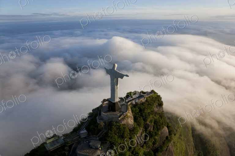High angle view of colossal Christ Redeemer statue surrounded by clouds, Corcovado,…