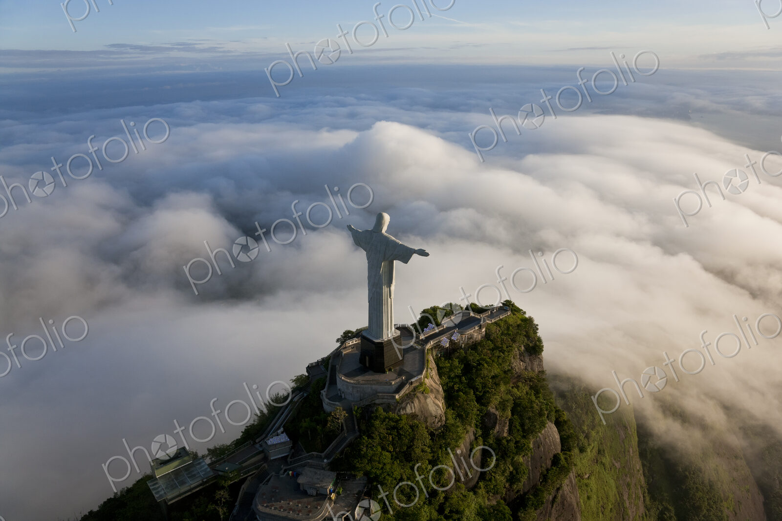 High angle view of colossal Christ Redeemer statue surrounded by clouds, Corcovado,…