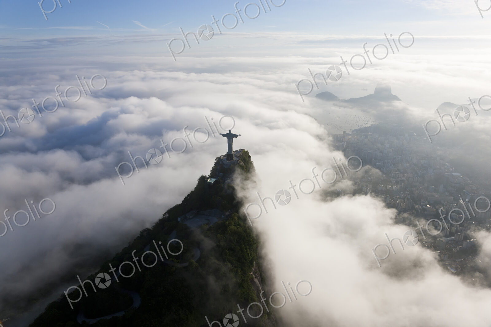 High angle view of colossal Christ Redeemer statue surrounded by clouds, Corcovado,…