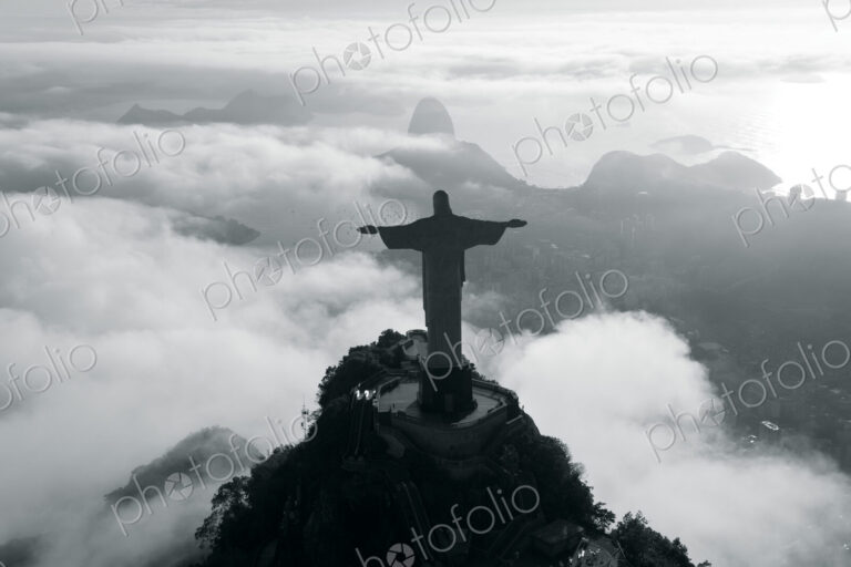 High angle view of colossal Christ Redeemer statue surrounded by clouds, Corcovado,…