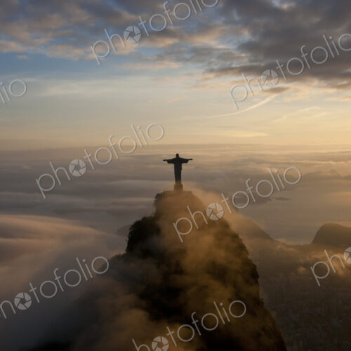High angle view of colossal Christ Redeemer statue surrounded by clouds at dusk,… High angle view of colossal Christ Redeemer statue surrounded by clouds at dusk,…