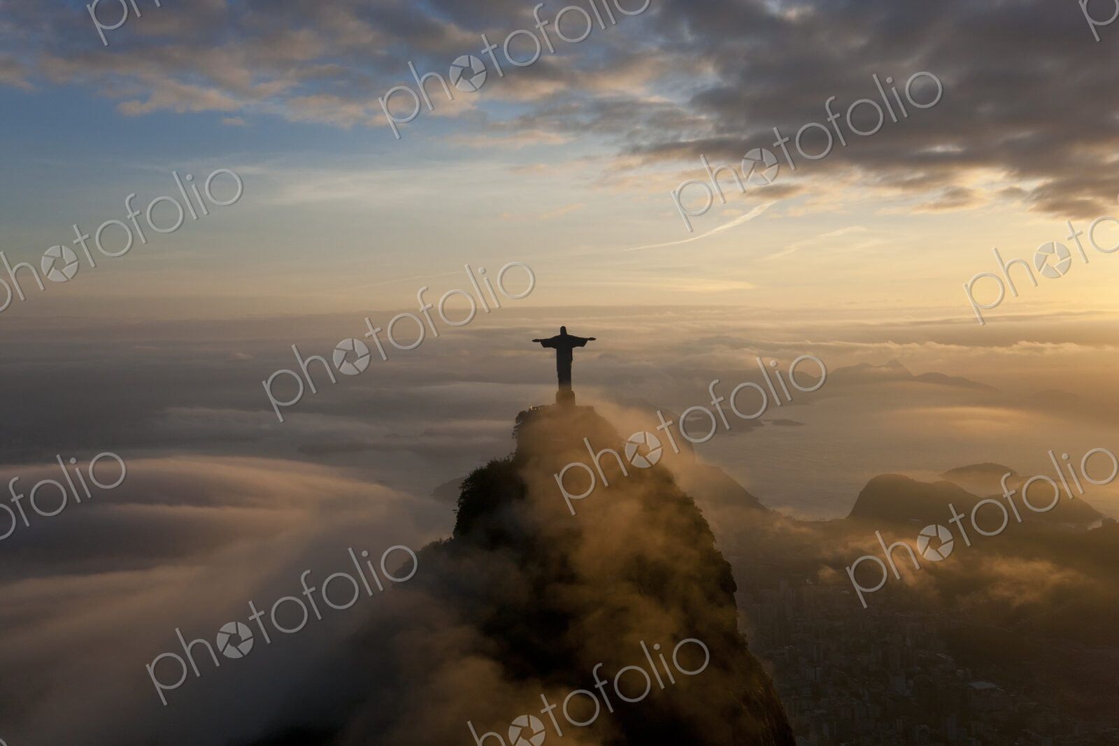 High angle view of colossal Christ Redeemer statue surrounded by clouds at dusk,…