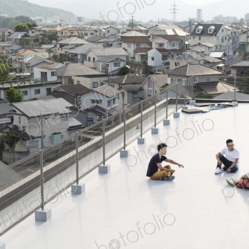 High angle view of group of young Japanese men and women sitting on a rooftop in an… High angle view of group of young Japanese men and women sitting on a rooftop in an…
