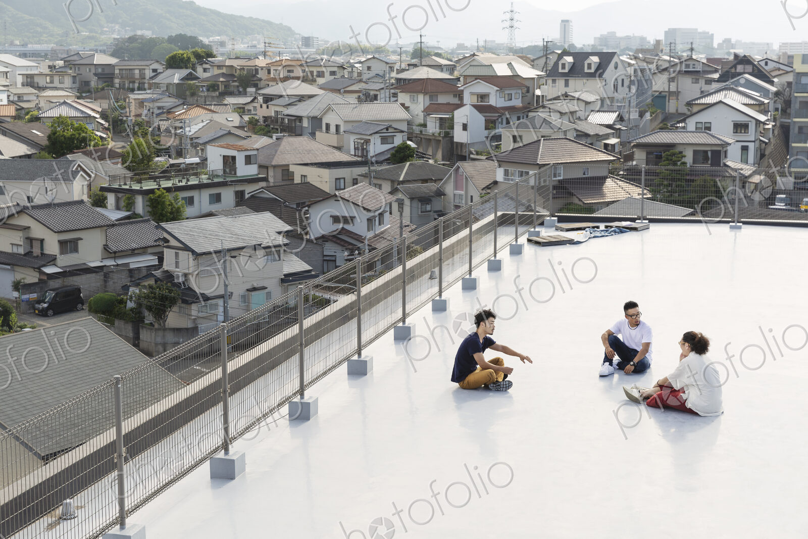 High angle view of group of young Japanese men and women sitting on a rooftop in an…