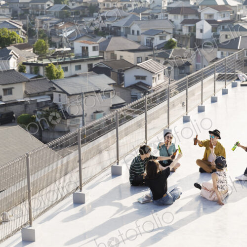 High angle view of group of young Japanese men and women sitting on a rooftop in an… High angle view of group of young Japanese men and women sitting on a rooftop in an…