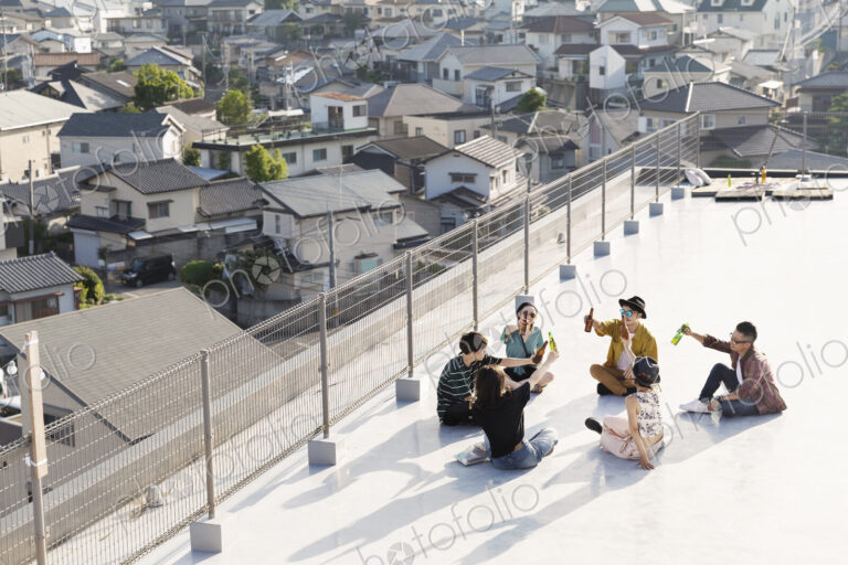 High angle view of group of young Japanese men and women sitting on a rooftop in an…