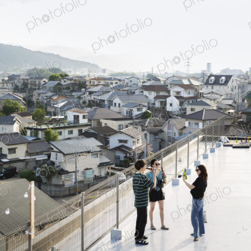 High angle view of group of young Japanese men and women standing on a rooftop in an… High angle view of group of young Japanese men and women standing on a rooftop in an…