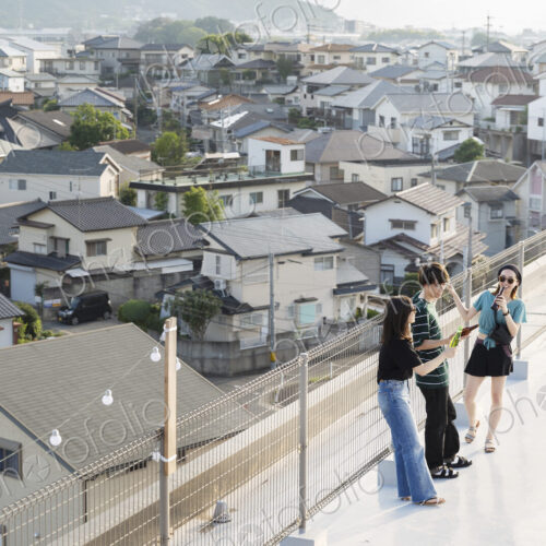 High angle view of group of young Japanese men and women standing on a rooftop in an… High angle view of group of young Japanese men and women standing on a rooftop in an…
