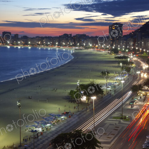 High angle view of long sandy beach lined by illuminated tall buildings, light trail… High angle view of long sandy beach lined by illuminated tall buildings, light trail…