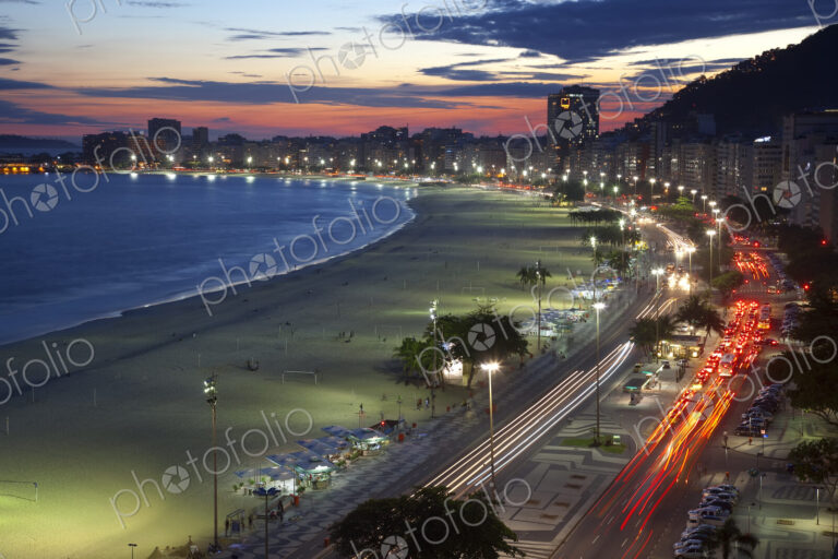 High angle view of long sandy beach lined by illuminated tall buildings, light trail…