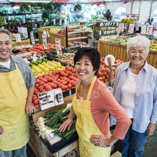 High angle view of man and two women wearing aprons standing at stall with fresh…