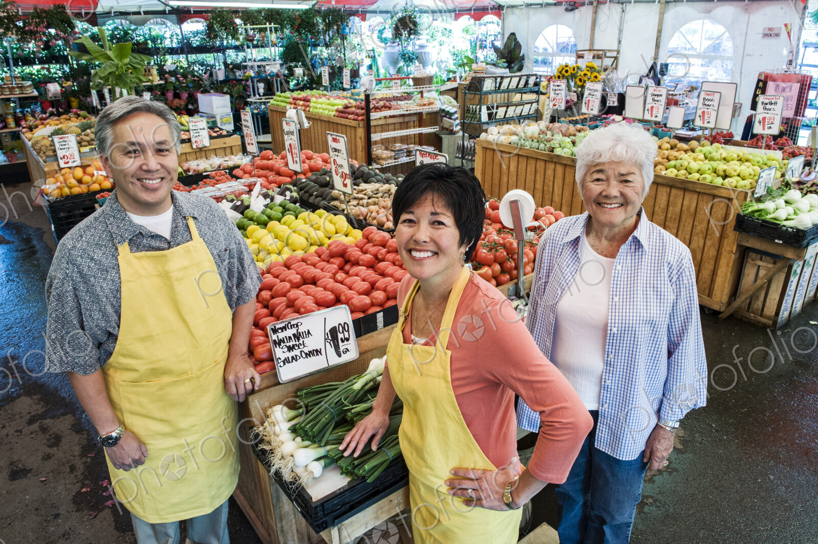High angle view of man and two women wearing aprons standing at stall with fresh…