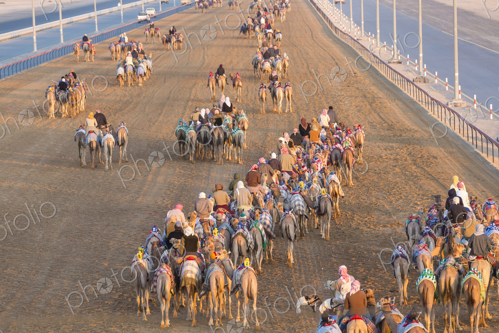 High angle view of people riding on camels with colourful saddles along a dusty road.