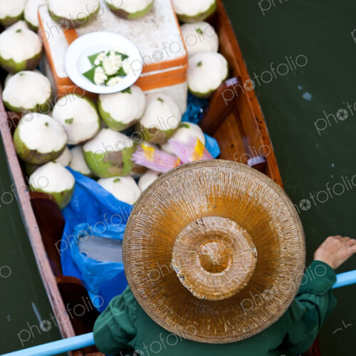 High angle view of person wearing hat sitting in narrow boat, transporting green coconuts.