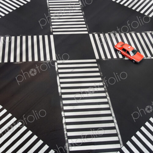High angle view of red car driving on urban road with pedestrian crossings. High angle view of red car driving on urban road with pedestrian crossings.