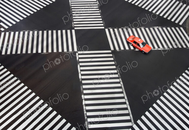 High angle view of red car driving on urban road with pedestrian crossings.