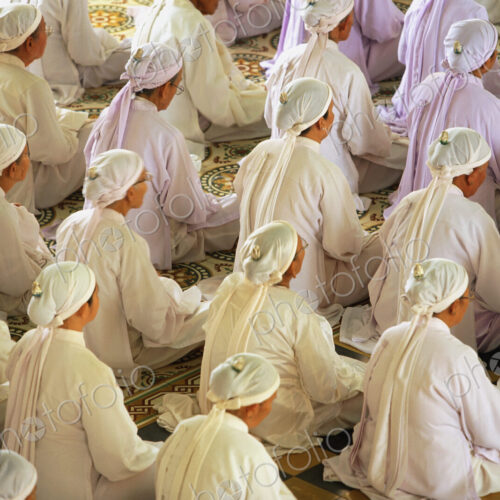 High angle view of rows of women wearing white robes and headscarves sitting on floor,…