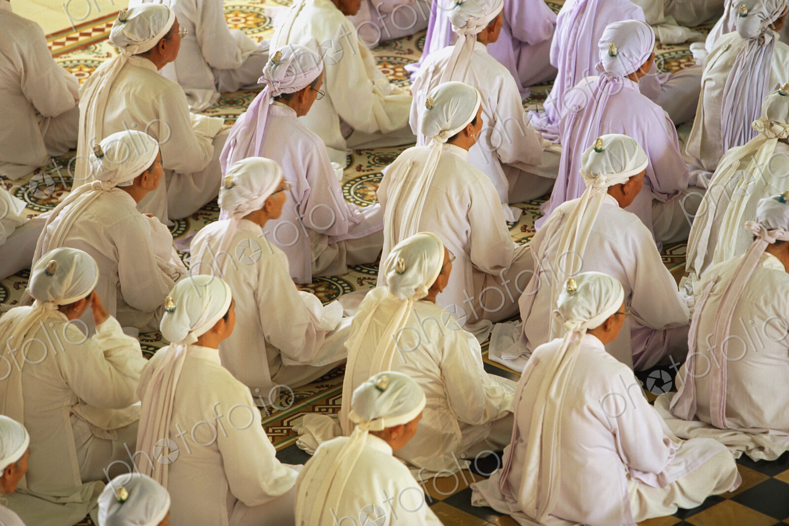 High angle view of rows of women wearing white robes and headscarves sitting on floor,…