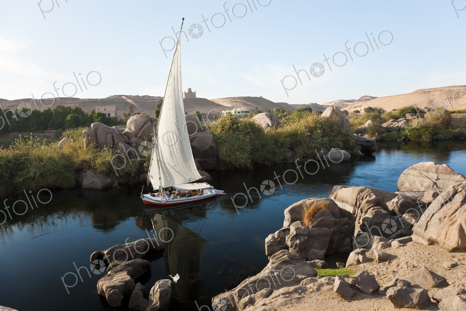 High angle view of sailboat on a river, rocks and sand hills in the distance.