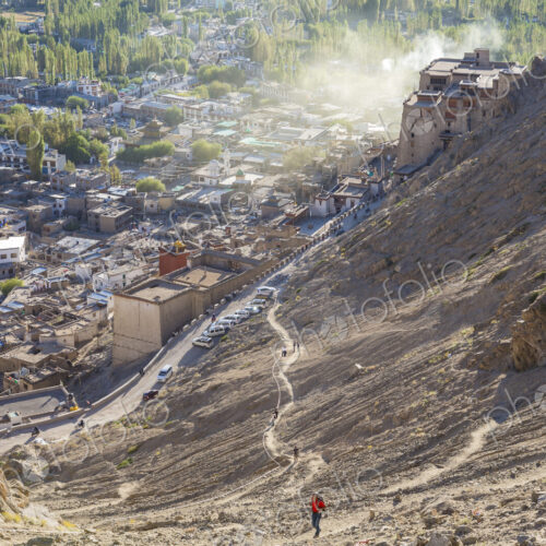High angle view of town with man climbing up dusty mountain slope.
