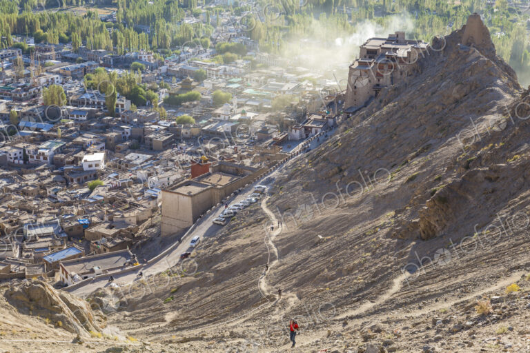 High angle view of town with man climbing up dusty mountain slope.