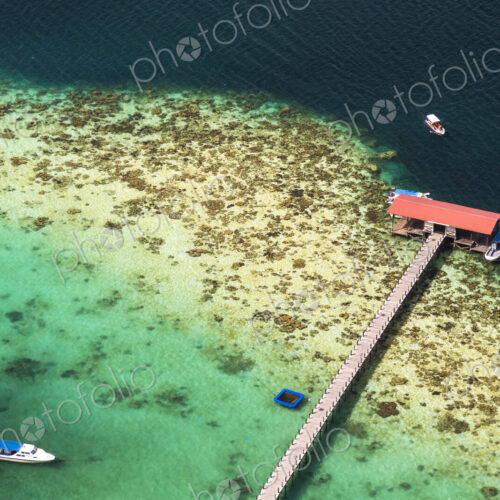 High angle view of tropical island, long pier and beach house, boats moored in the ocean. High angle view of tropical island, long pier and beach house, boats moored in the ocean.