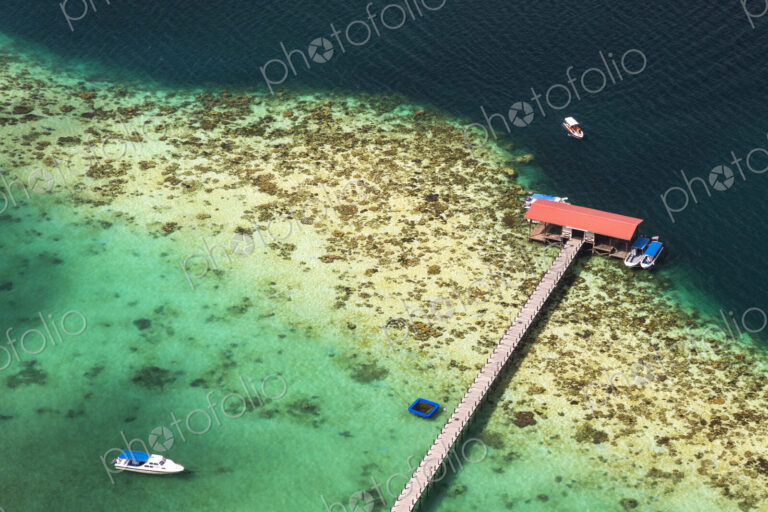 High angle view of tropical island, long pier and beach house, boats moored in the ocean.