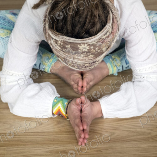 High angle view of woman wearing white blouse and headscarf sitting on floor in yoga pose.